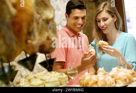 Couple drinking wine and eating tapas. Pintxos. Bar txondorra. Parte Vieja. Old town. San Sebastian. Donostia. Gipuzkoa. Basque Country. Spain. Stock Photo