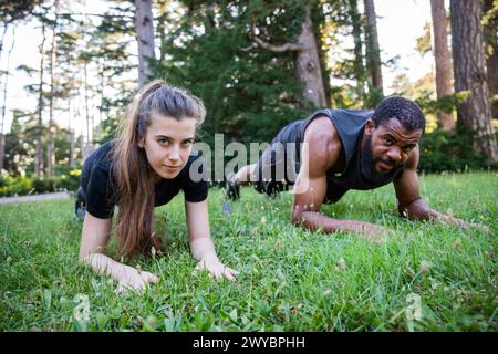 A man and a woman are doing pushups on a grassy field. The woman is on her knees and the man is on his hands and knees Stock Photo