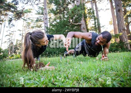 A man and a woman are doing a plank exercise on a grassy field. The man is wearing a black shirt and the woman is wearing a black shirt Stock Photo