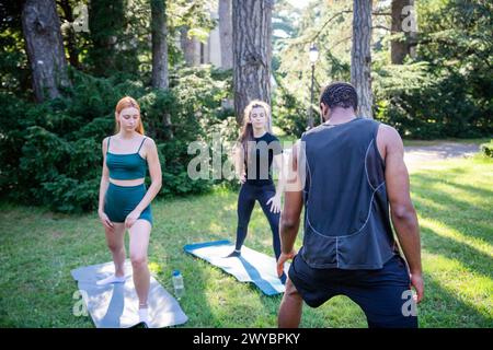 A man and two women are exercising in a park, personal trainer is working with his clients Stock Photo