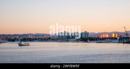 Twilight over Marina del Rey, a serene evening with urban city buildings in silhouette and a pleasure boat sailing on calm water Stock Photo