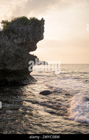 A serene sunset viewed from behind textured rocks of a coastal landscape Stock Photo