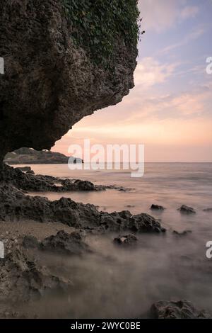 A serene sunset viewed from behind textured rocks of a coastal landscape Stock Photo