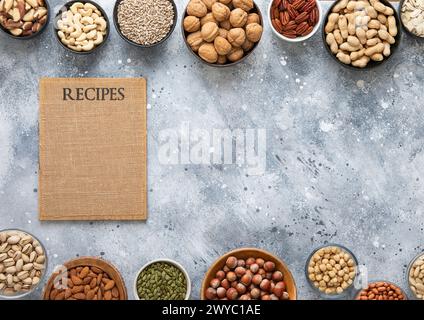 Mixed assorted nuts and seeds in various bowls on light kitchen table with recipe board. Stock Photo