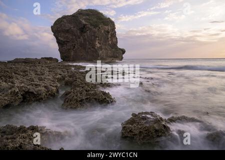 A serene sunset with a rocky outcrop standing tall amid a silky sea with a long exposure effect Stock Photo