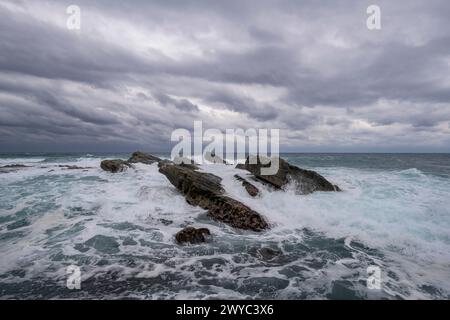 Captivating rock formations against the backdrop of powerful, white-capped sea waves under a stormy sky Stock Photo