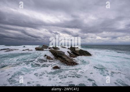 Captivating rock formations against the backdrop of powerful, white-capped sea waves under a stormy sky Stock Photo