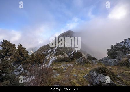 The peak of a mountain barely visible through dispersing clouds, creating an ethereal landscape of mystery Stock Photo