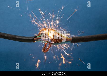 Sparks explosion between electrical cables, on blue background, fire hazard concept Stock Photo