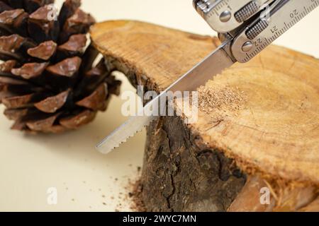 Swiss army pocket knife sawing a wooden log on beige background, soft focus Stock Photo
