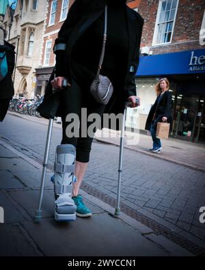 A lady on crutches shopping on the high street. Stock Photo