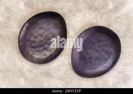 Pair of empty black irregularly shaped plates on beige concrete background. Top view, with copy space Stock Photo
