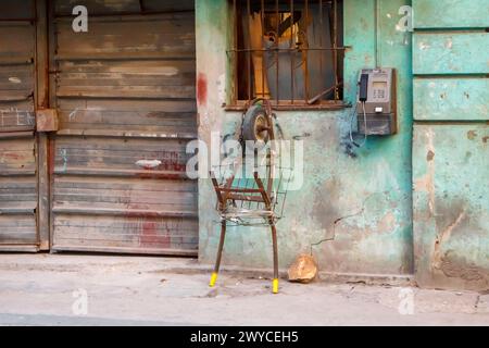 Rustic rusty wheelbarrow cart in a dirty weathered wall with a payphone in Havana, Cuba Stock Photo