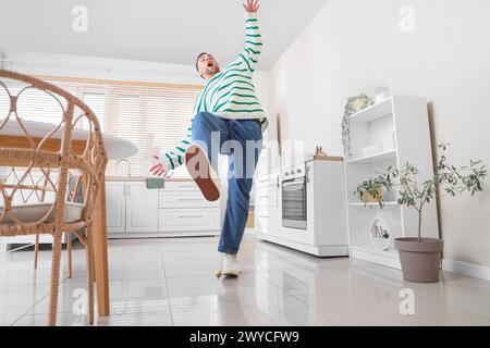 Young man falling after slipping on banana peel in kitchen Stock Photo