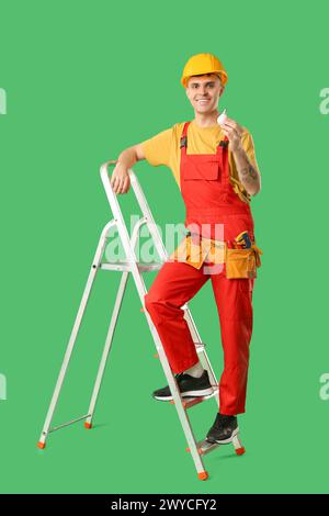 Young male electrician on stepladder with LED lamp against green background Stock Photo