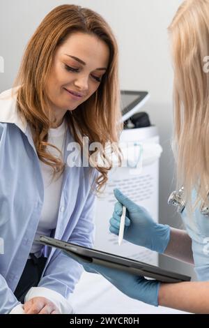 Study of tests: A woman learns the results of the examination from a doctor who explains important aspects of the diagnosis on a tablet and provides Stock Photo