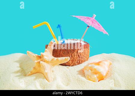 Coconut with a straw, shells, starfish and a sun umbrella on the sand. Summer background, concept of relaxation and vacation. Stock Photo