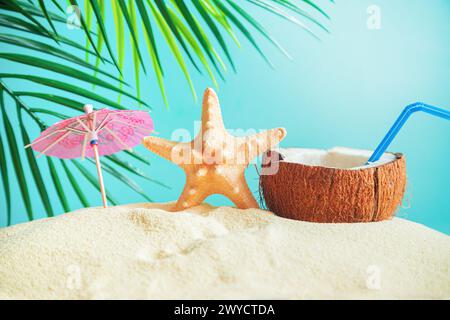 Coconut with a straw, shells, starfish and a sun umbrella on the sand. Summer background, concept of relaxation and vacation. Stock Photo