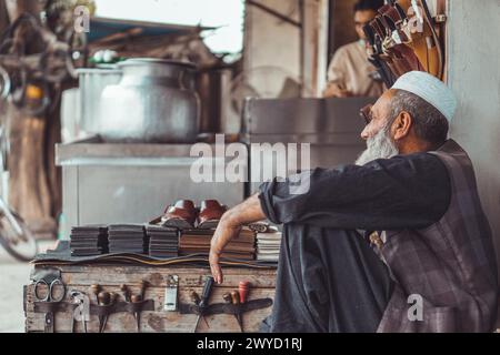 Poor old Pakistani Pathan shoe man cobbler on the local streets of Pakistan with his hand made leather shoes and repair tools in his street shop Stock Photo