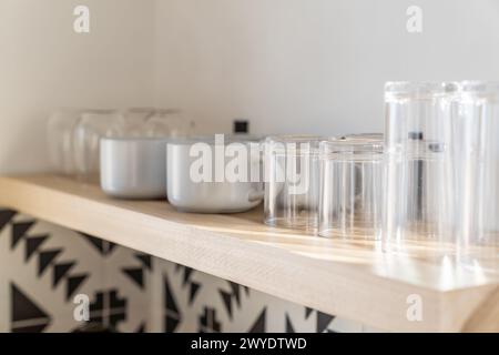 Coffee cups and glasses on a wood floating shelf in a modern kitchen with black and white tile Stock Photo