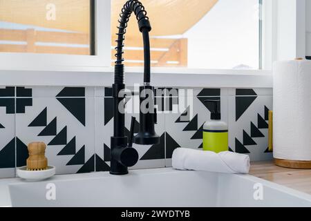Faucet sink and soap dispenser at a kitchen window in a modern kitchen with black and white tile Stock Photo
