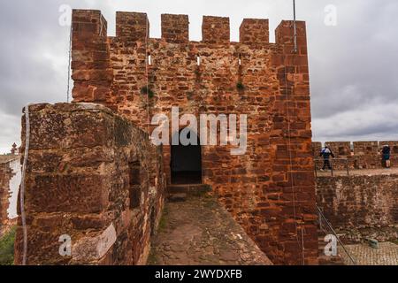 Terracotta-tiled rooftops of Silves Castle with the Portuguese flag, overlooking a vast landscape. Stock Photo