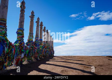 A row of wooden pillars wrapped with multi-coloured ribbons as a worship practice for the Buryats are seen near the Shamanka Rock on Lake Baikal, Siberia. Meter-thick blue ice of frozen Lake Baikal has become a winter tourist attraction over the years, where visitors usually travel to the third-largest lake island in the world, Olkhon Island, to observe the deepest lake in the world. Given to the prolonged Russian war on Ukraine and the subsequent international sanctions since 2022, number of visitors to the island has been dwindled which a majority of tourists are from China. Stock Photo