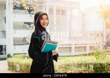 University saudi muslim niqab woman high education in university campus happy smiling with modern knowledge book. Arab saudi black chador lady. Stock Photo