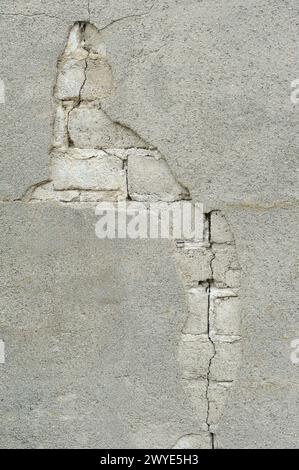 A damaged wall with cracks in the plaster revealing underlying brick structure. Stock Photo