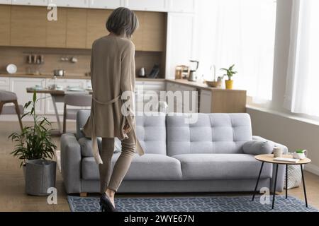 Woman walking towards the sofa, rear view Stock Photo