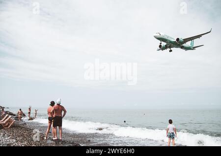 Batumi, Georgia - 15th august, 2022: Back view tourist on beach watch commercial airplane land in real time to Batumi airport runway by sea Stock Photo