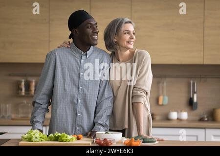 Happy multiethnic couple standing in kitchen looking away and smiling Stock Photo