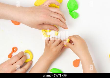 High angle shot of boy and a teacher or mother playing with colorful modeling compound on the table Stock Photo
