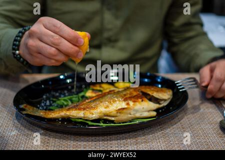 Man squeezing a lemon over a plate of roaster fish Stock Photo