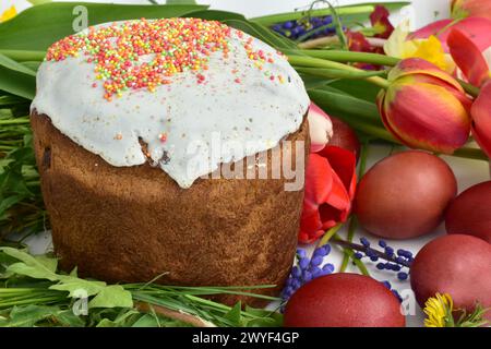 The picture shows a close-up of a tall Easter cake with a white top and flowers lying around it, captured against a white background. Stock Photo