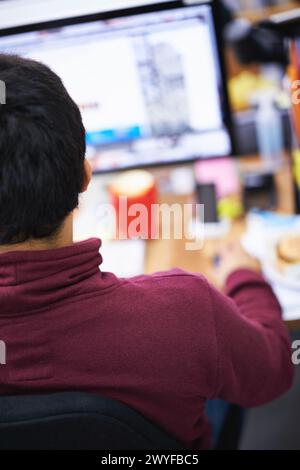 Rear view, IT employee and computer in office with software for information technology, web development and programming. Young person or man with Stock Photo