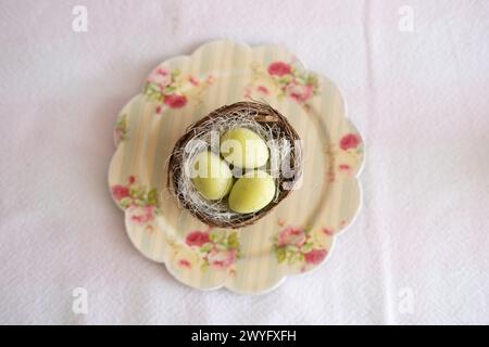 Top view of a small plate with a small nest containing three Easter eggs on an Easter candy table. Typical Easter sweets on a festive celebration tabl Stock Photo