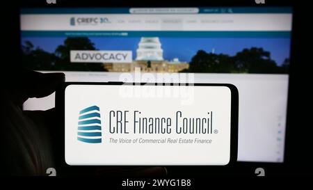 Person holding cellphone with logo of trade association CRE Finance Council (CREFC) in front of business webpage. Focus on phone display. Stock Photo