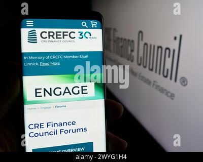 Person holding cellphone with webpage of trade association CRE Finance Council (CREFC) in front of logo. Focus on center of phone display. Stock Photo