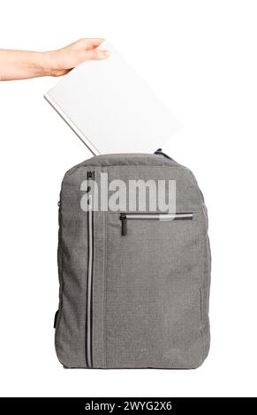 Hand putting blank book cover mockup, textbook mock up into schoolbag, backpack isolated on white. Stock Photo
