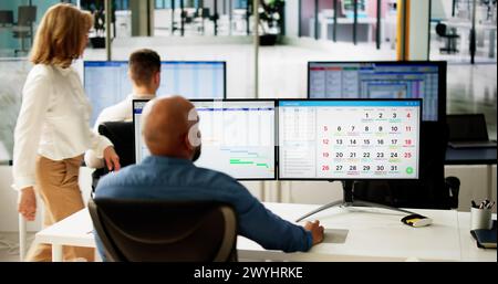 Young Businesspeople Analyzing Gantt Chart And Calendar On Computer In Office Stock Photo