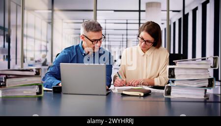 Two Businesspeople Calculating Invoice In Office While Using Laptop Stock Photo