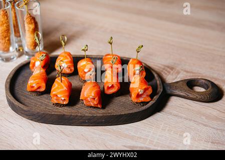 Elegant smoked salmon rolls filled with cream cheese on dark rye bread, served on a rustic wooden board. Stock Photo