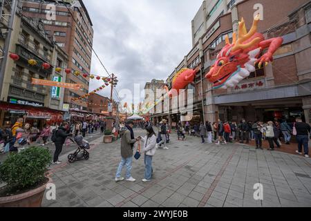 Busy street captured in broad daylight with a large Chinese dragon decoration overhead, people shopping for the Chinese New Year Stock Photo