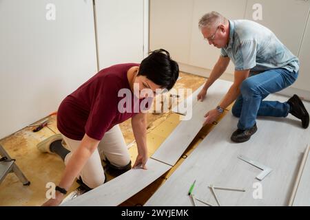 Senior couple installing laminate flooring in their new home together. DIY concept. Mature woman and man doing renovation. Stock Photo