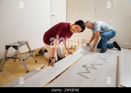 Senior couple installing laminate flooring in their new home together. DIY concept. Mature woman and man doing renovation. Stock Photo