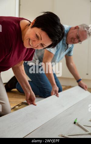 Senior couple installing laminate flooring in their new home together. DIY concept. Mature woman and man doing renovation. Stock Photo