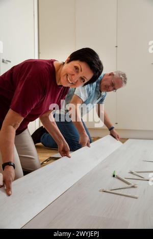 Senior couple installing laminate flooring in their new home together. DIY concept. Mature woman and man doing renovation. Stock Photo