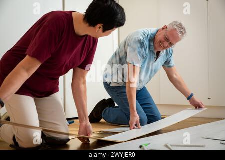 Senior couple installing laminate flooring in their new home together. DIY concept. Mature woman and man doing renovation. Stock Photo
