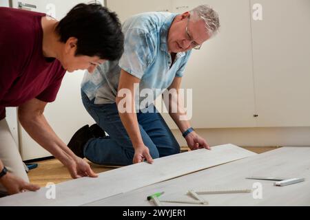 Senior couple installing laminate flooring in their new home together. DIY concept. Mature woman and man doing renovation. Stock Photo